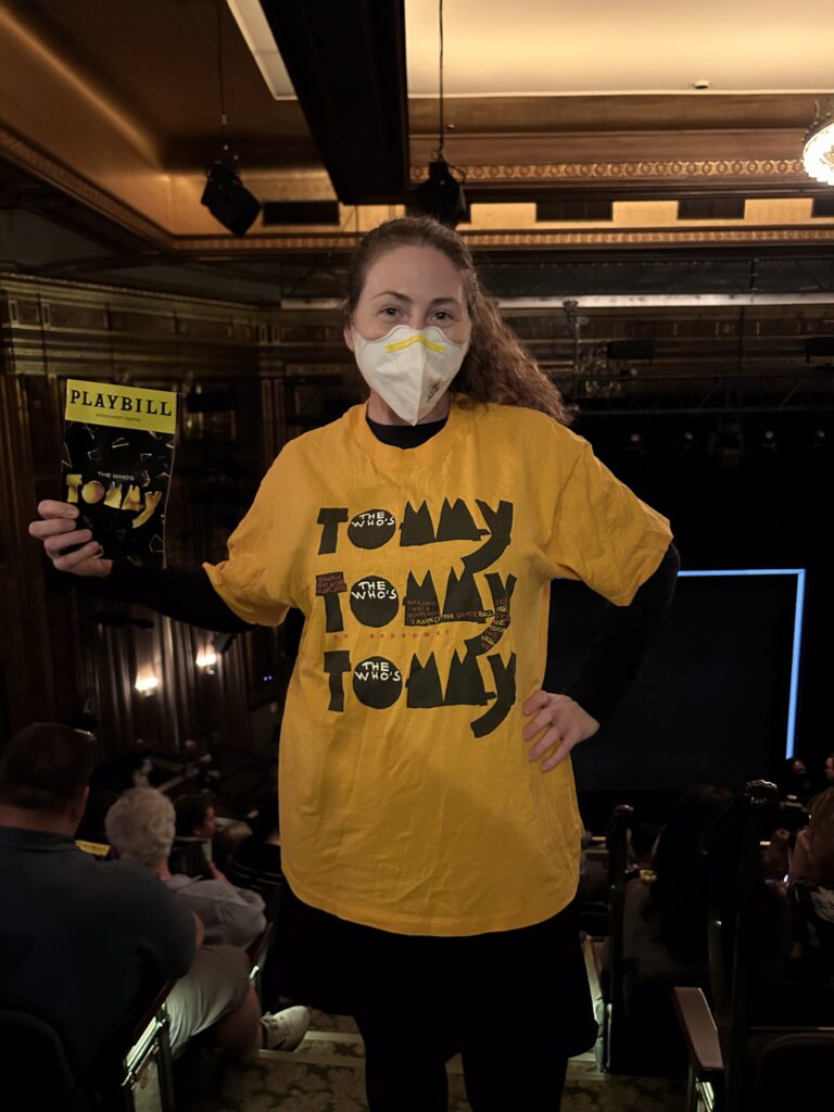 Shoshana wearing a 1990s Tommy shirt holding the Tommy revival program.